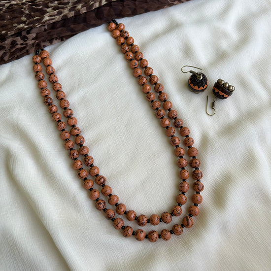 A two-layered terracotta bead necklace with adjustable thread, displayed alongside a matching pair of earrings, laid out on a white fabric.