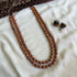 A two-layered terracotta bead necklace with adjustable thread, displayed alongside a matching pair of earrings, laid out on a white fabric.