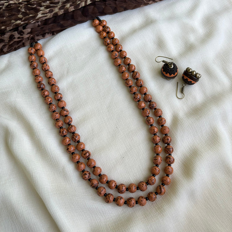 A two-layered terracotta bead necklace with adjustable thread, displayed alongside a matching pair of earrings, laid out on a white fabric.