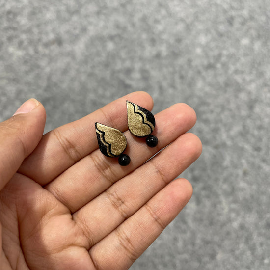 Handmade gold and black thilak clay stud earrings with a bead drop
